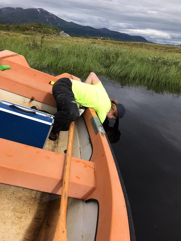 Cheristy leaning over the side of a boat, shoulder deep sampling a stream